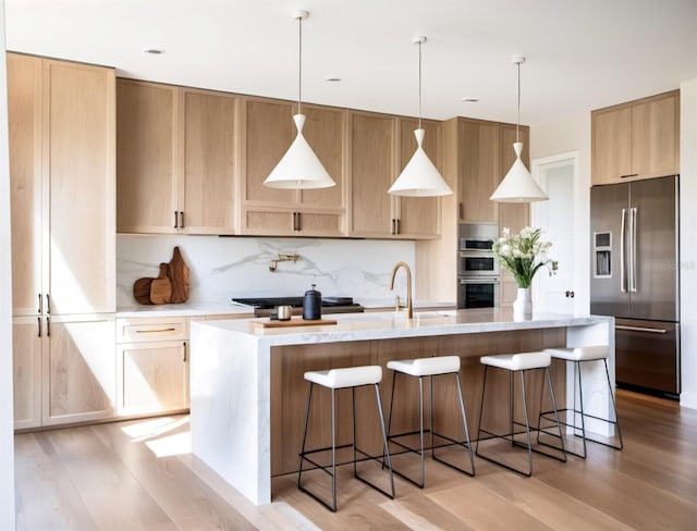 kitchen featuring decorative light fixtures, appliances with stainless steel finishes, light hardwood / wood-style floors, and a kitchen island with sink