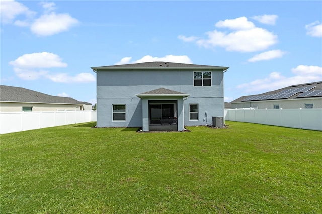 rear view of property featuring cooling unit, a yard, and solar panels