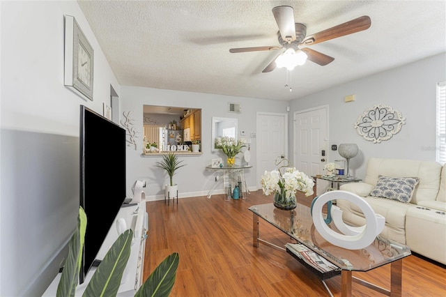 living area featuring a ceiling fan, a textured ceiling, baseboards, and wood finished floors