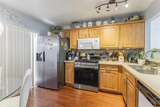 kitchen with light wood finished floors, decorative backsplash, appliances with stainless steel finishes, light countertops, and a sink