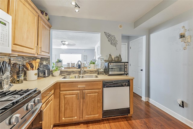 kitchen with white appliances, a sink, light countertops, decorative backsplash, and dark wood finished floors