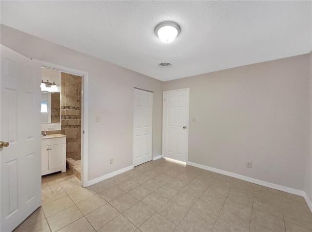 unfurnished bedroom featuring connected bathroom, a closet, a textured ceiling, and light tile patterned flooring