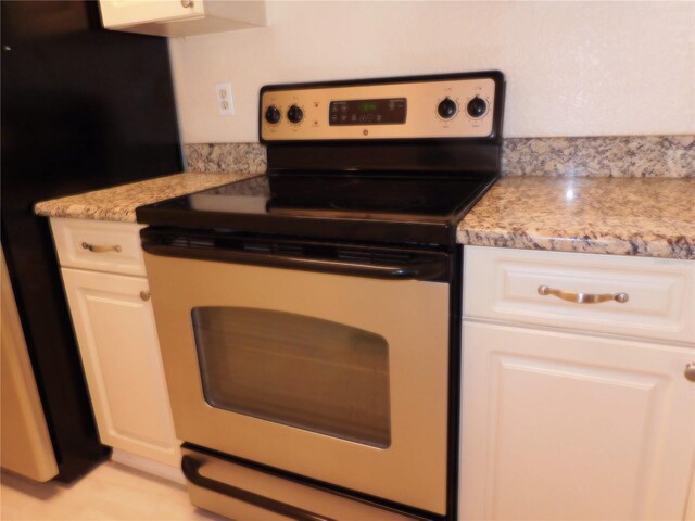 kitchen featuring stainless steel electric range oven, black refrigerator, white cabinets, and light stone counters