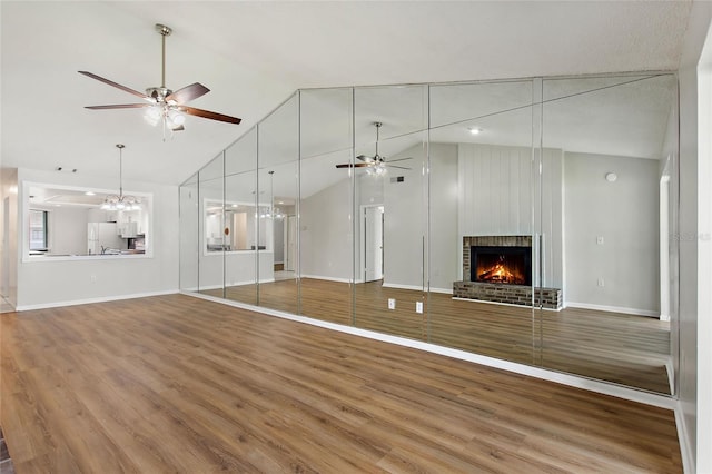 unfurnished living room featuring light hardwood / wood-style floors, a fireplace, ceiling fan with notable chandelier, and high vaulted ceiling