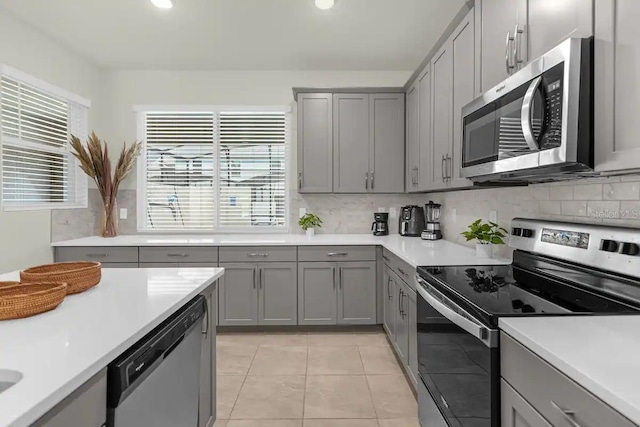 kitchen featuring light tile patterned flooring, tasteful backsplash, appliances with stainless steel finishes, and gray cabinetry