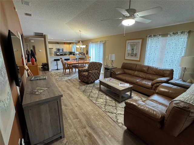 living room featuring ceiling fan, light hardwood / wood-style floors, and a textured ceiling