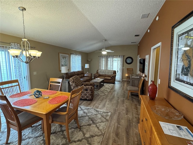 dining space featuring dark hardwood / wood-style flooring, ceiling fan with notable chandelier, vaulted ceiling, and a textured ceiling