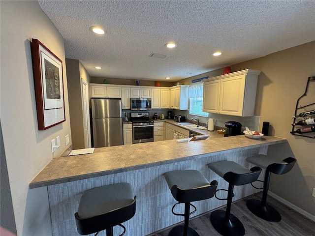 kitchen featuring appliances with stainless steel finishes, sink, a kitchen breakfast bar, kitchen peninsula, and a textured ceiling