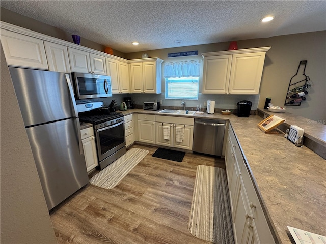 kitchen featuring appliances with stainless steel finishes, sink, light hardwood / wood-style flooring, and a textured ceiling