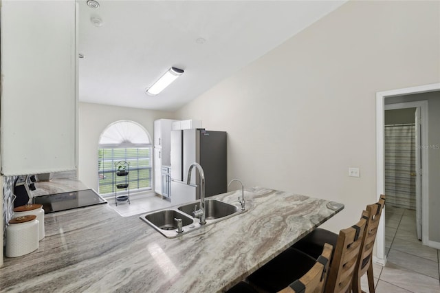 kitchen featuring a kitchen breakfast bar, vaulted ceiling, sink, range, and stainless steel refrigerator