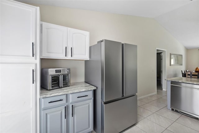 kitchen with lofted ceiling, light tile patterned floors, appliances with stainless steel finishes, white cabinetry, and light stone counters