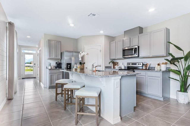 kitchen with light tile patterned flooring, a kitchen island with sink, gray cabinets, appliances with stainless steel finishes, and sink