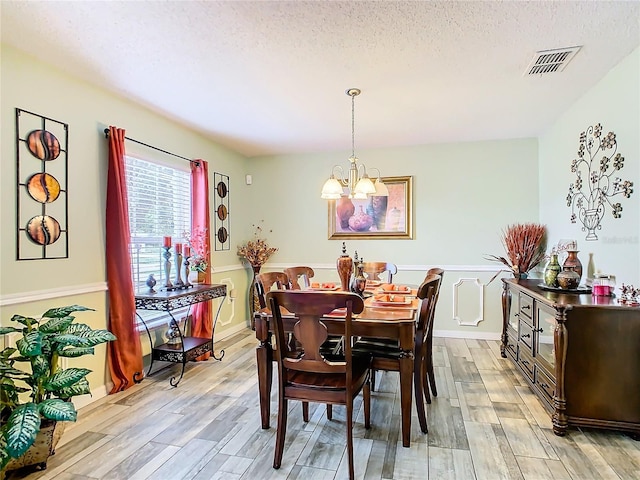 dining room with a textured ceiling, light hardwood / wood-style flooring, and a chandelier