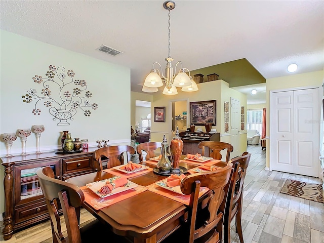 dining room with a textured ceiling, an inviting chandelier, and light hardwood / wood-style floors