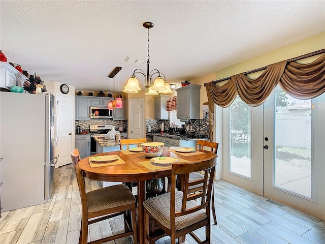 dining area with french doors, an inviting chandelier, a textured ceiling, and light wood-type flooring