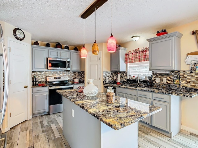 kitchen with appliances with stainless steel finishes, backsplash, gray cabinetry, pendant lighting, and a center island