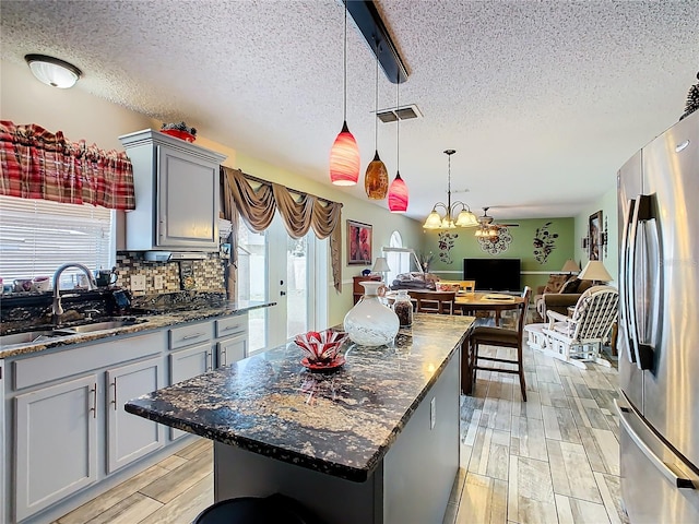 kitchen with stainless steel fridge, backsplash, gray cabinets, a textured ceiling, and a center island