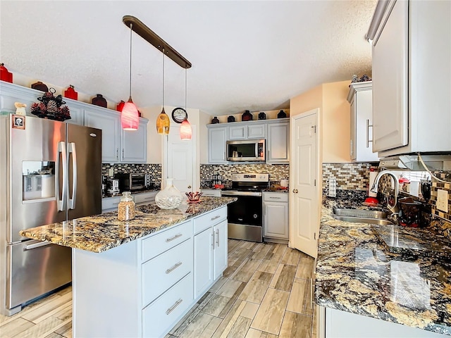 kitchen featuring sink, a center island, appliances with stainless steel finishes, tasteful backsplash, and hanging light fixtures