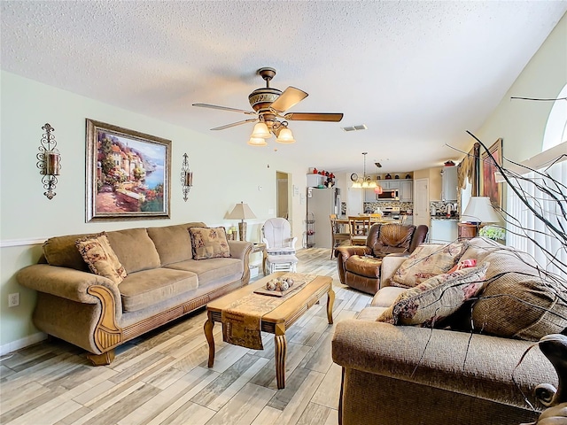 living room with ceiling fan, a textured ceiling, and light hardwood / wood-style flooring