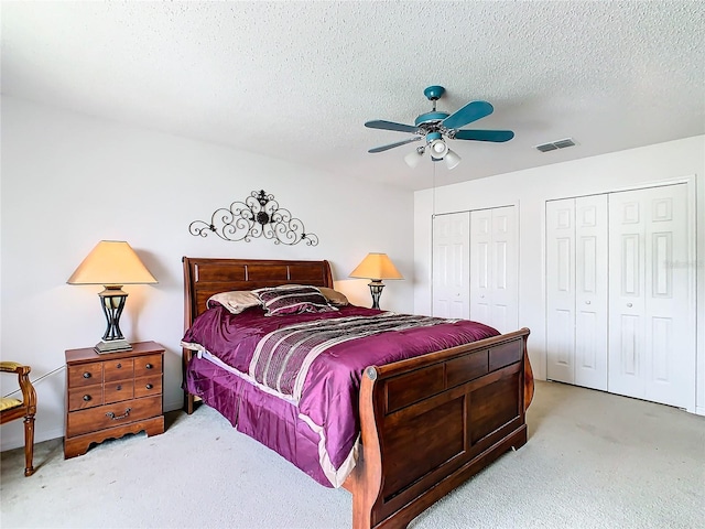 carpeted bedroom featuring ceiling fan, a textured ceiling, and multiple closets