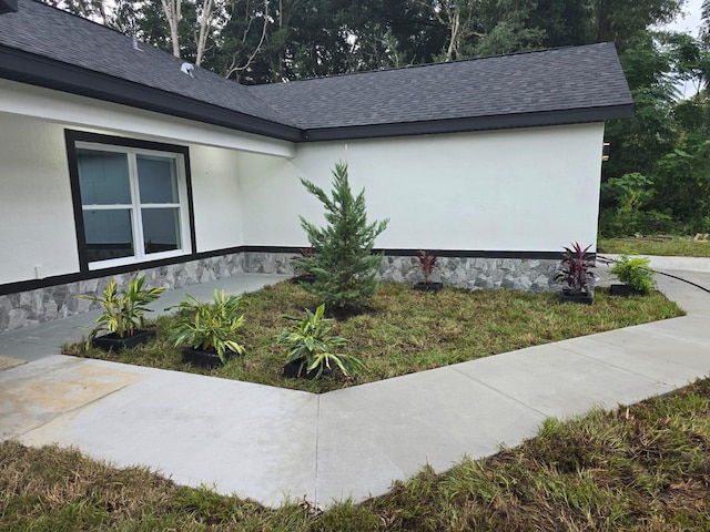 view of side of property featuring roof with shingles and stucco siding