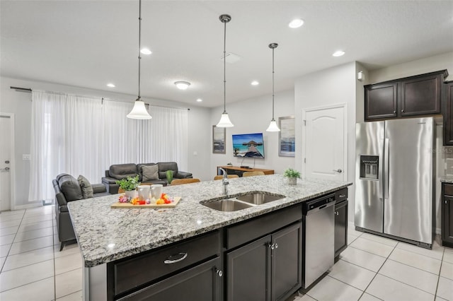 kitchen featuring appliances with stainless steel finishes, an island with sink, light stone countertops, light tile patterned floors, and sink