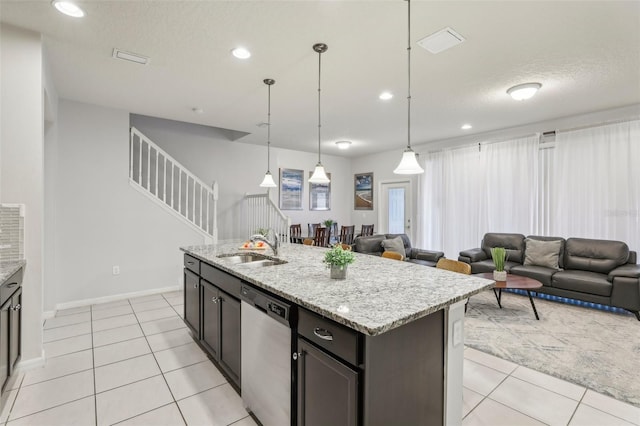 kitchen featuring light stone counters, stainless steel dishwasher, light tile patterned floors, a center island with sink, and sink