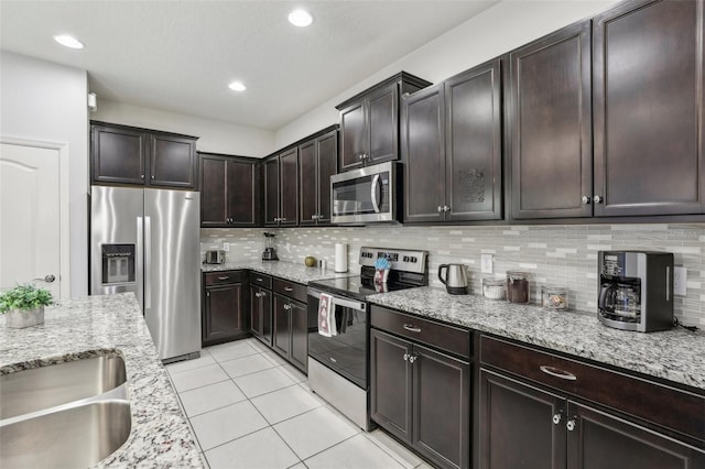 kitchen with appliances with stainless steel finishes, backsplash, light tile patterned floors, light stone counters, and dark brown cabinets