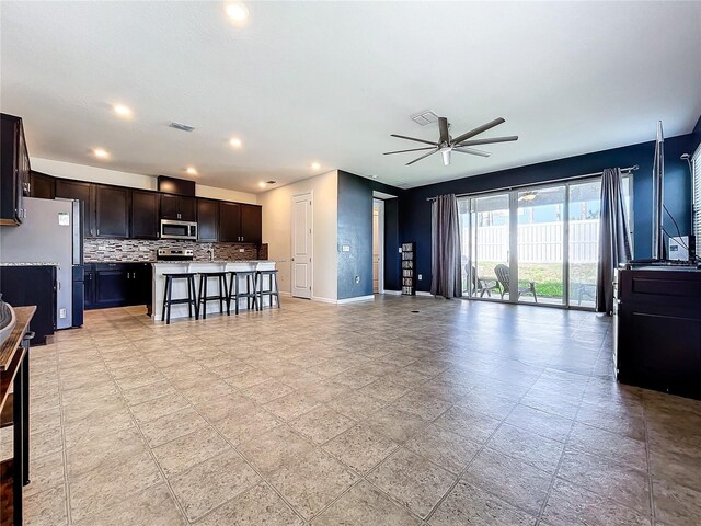 kitchen featuring a center island, a kitchen breakfast bar, ceiling fan, appliances with stainless steel finishes, and tasteful backsplash