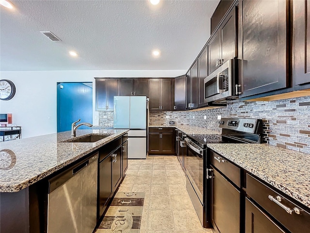 kitchen featuring sink, an island with sink, tasteful backsplash, dark brown cabinetry, and stainless steel appliances