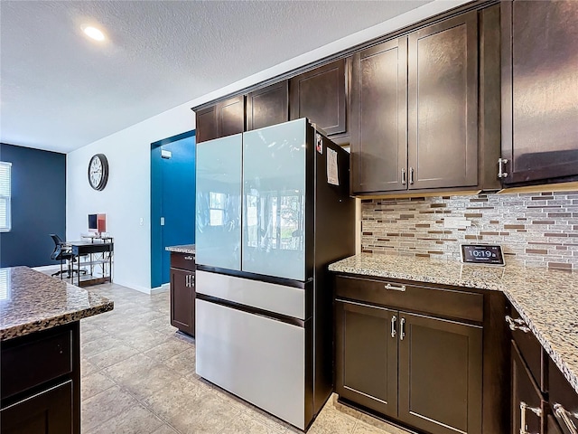 kitchen featuring light stone countertops, dark brown cabinetry, tasteful backsplash, and stainless steel refrigerator