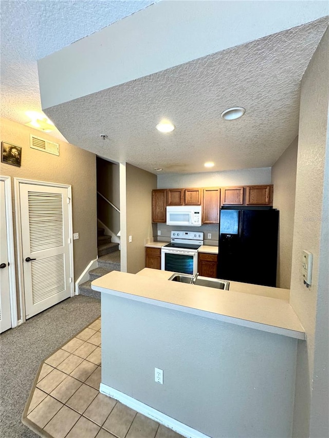 kitchen featuring a textured ceiling, kitchen peninsula, white appliances, and light tile patterned floors