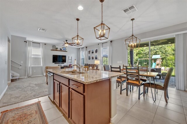 kitchen with sink, light stone counters, decorative light fixtures, stainless steel dishwasher, and a kitchen island with sink