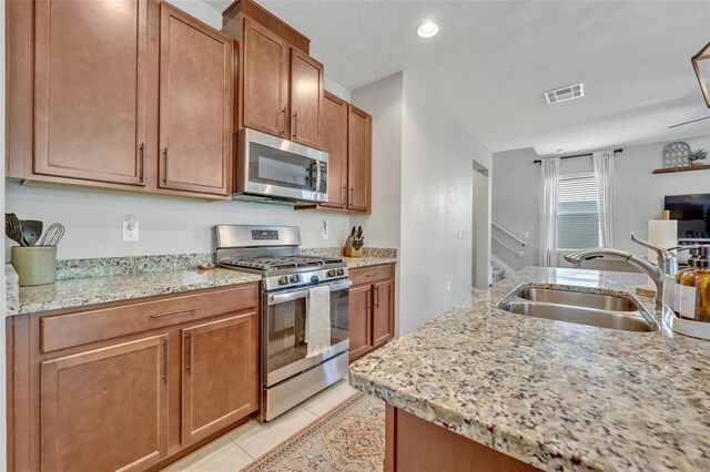 kitchen with light tile patterned flooring, appliances with stainless steel finishes, sink, and light stone counters