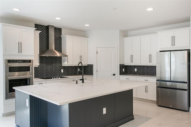 kitchen with stainless steel appliances, wall chimney range hood, an island with sink, and white cabinets