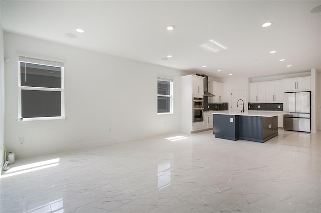 kitchen featuring a kitchen island with sink, stainless steel appliances, white cabinets, and tasteful backsplash