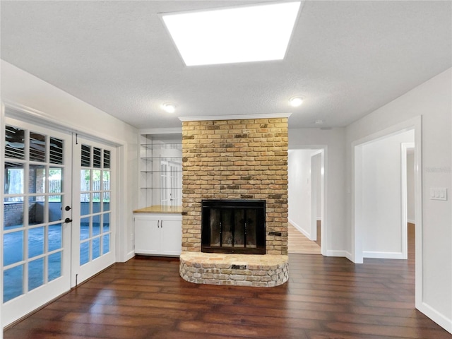 unfurnished living room featuring dark hardwood / wood-style flooring, french doors, a brick fireplace, and a textured ceiling