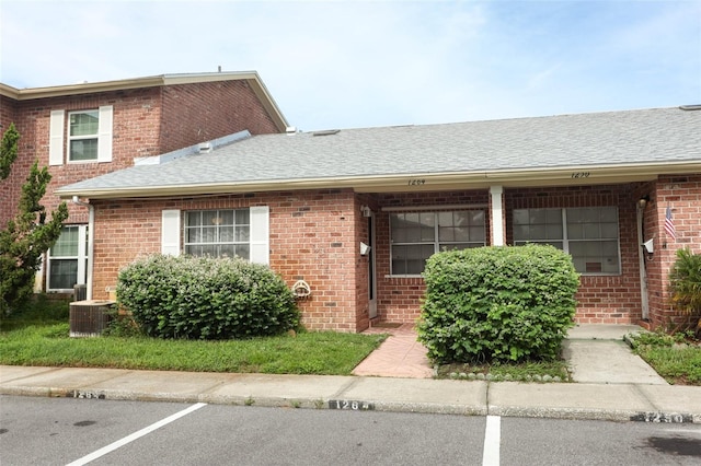 view of front facade with a shingled roof, uncovered parking, brick siding, and central AC