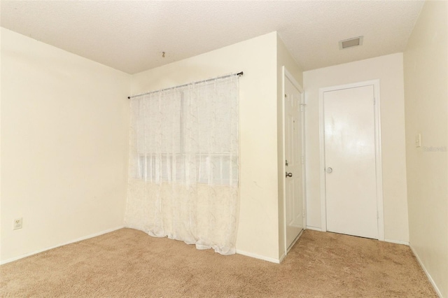 empty room featuring a textured ceiling, visible vents, and light colored carpet