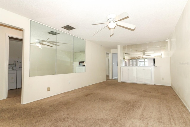 carpeted spare room with washing machine and dryer, visible vents, and a ceiling fan