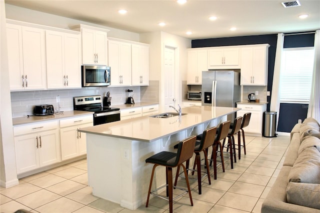 kitchen featuring stainless steel appliances, backsplash, a kitchen island with sink, and a kitchen bar