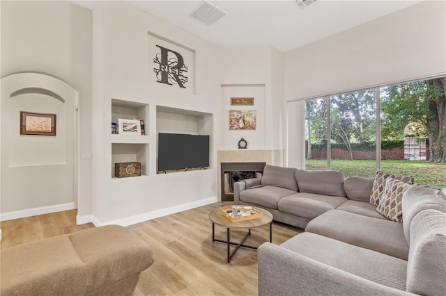 living room with a towering ceiling, built in features, and light wood-type flooring