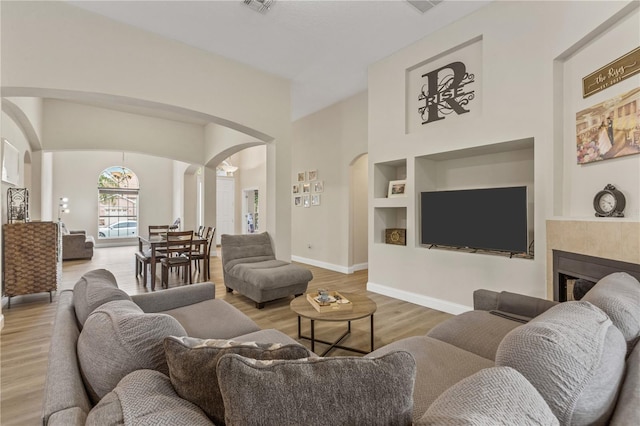 living room with decorative columns, built in shelves, a tile fireplace, and light wood-type flooring