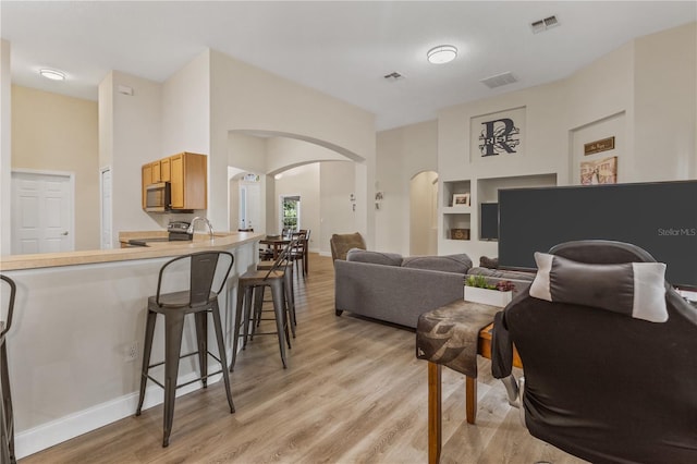 living room featuring built in features, light hardwood / wood-style flooring, and sink