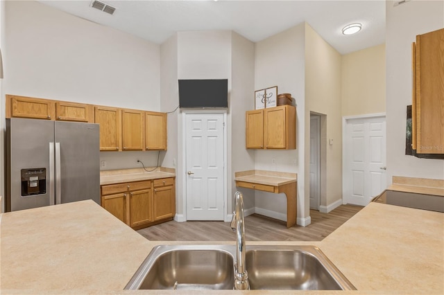 kitchen with stainless steel fridge, sink, a towering ceiling, and light wood-type flooring