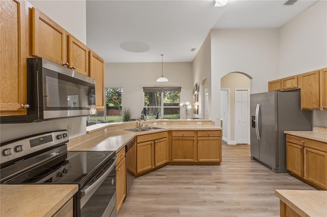 kitchen with stainless steel appliances, sink, pendant lighting, a high ceiling, and light wood-type flooring