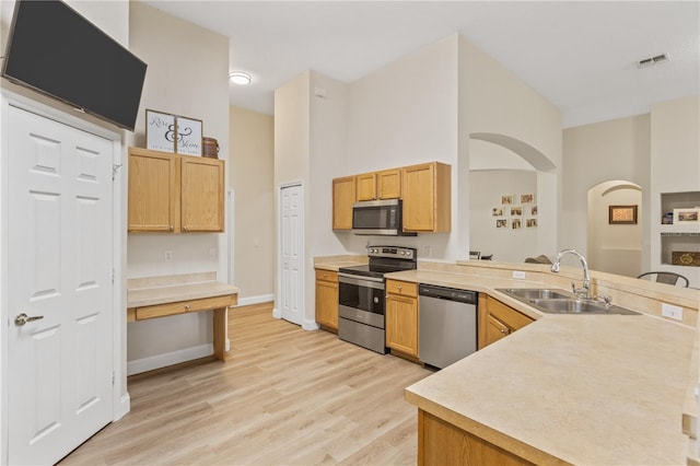 kitchen featuring sink, a towering ceiling, light wood-type flooring, and stainless steel appliances