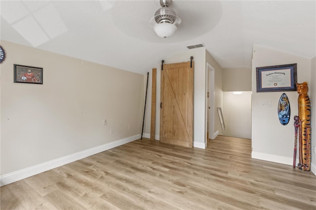 unfurnished living room with light wood-type flooring, ceiling fan, lofted ceiling, and a barn door