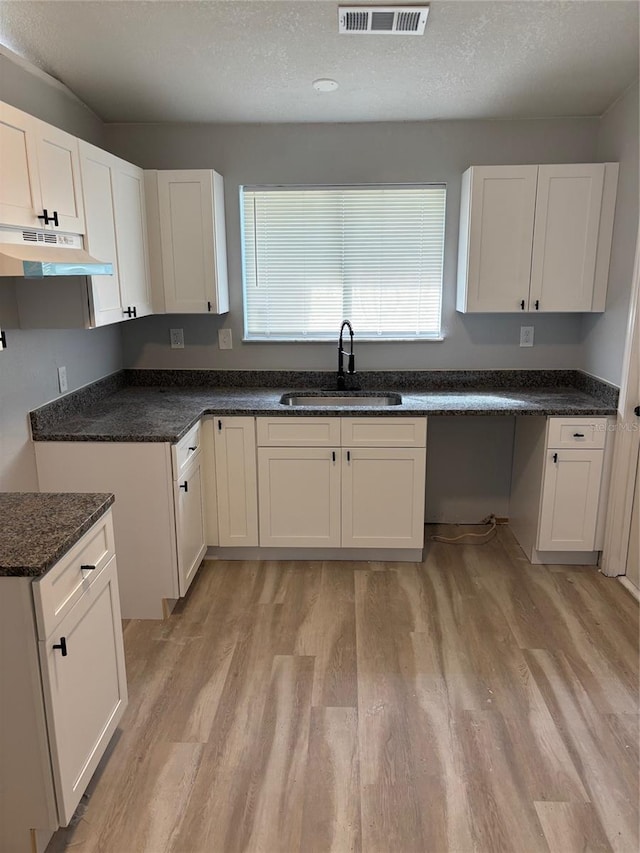 kitchen featuring white cabinetry, a textured ceiling, light hardwood / wood-style flooring, dark stone countertops, and sink