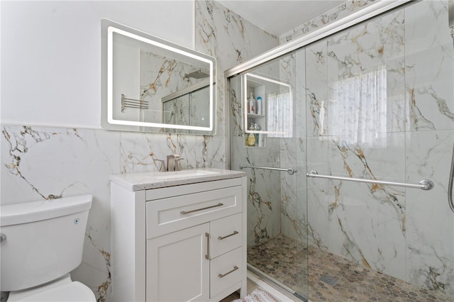 bathroom with tile walls, a shower with door, vanity, and toilet